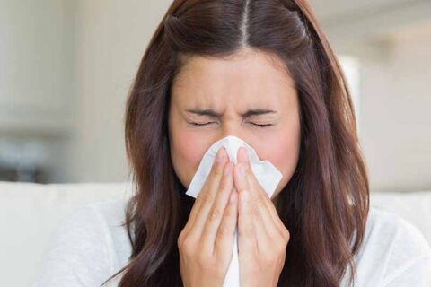 Woman sneezing into tissue indoors
