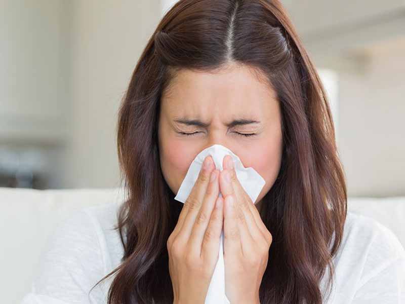 Woman sneezing into tissue indoors